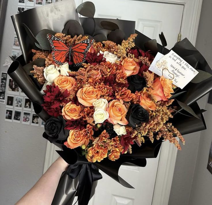Bouquet of flowers with a butterfly and a card, held by a person.