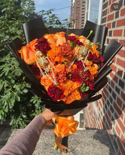 Bouquet with orange and red flowers and skeleton decorations held by a person outdoors.
