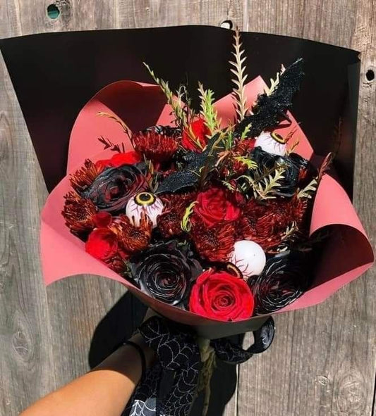 Bouquet of red and black flowers wrapped in pink paper on a wooden surface